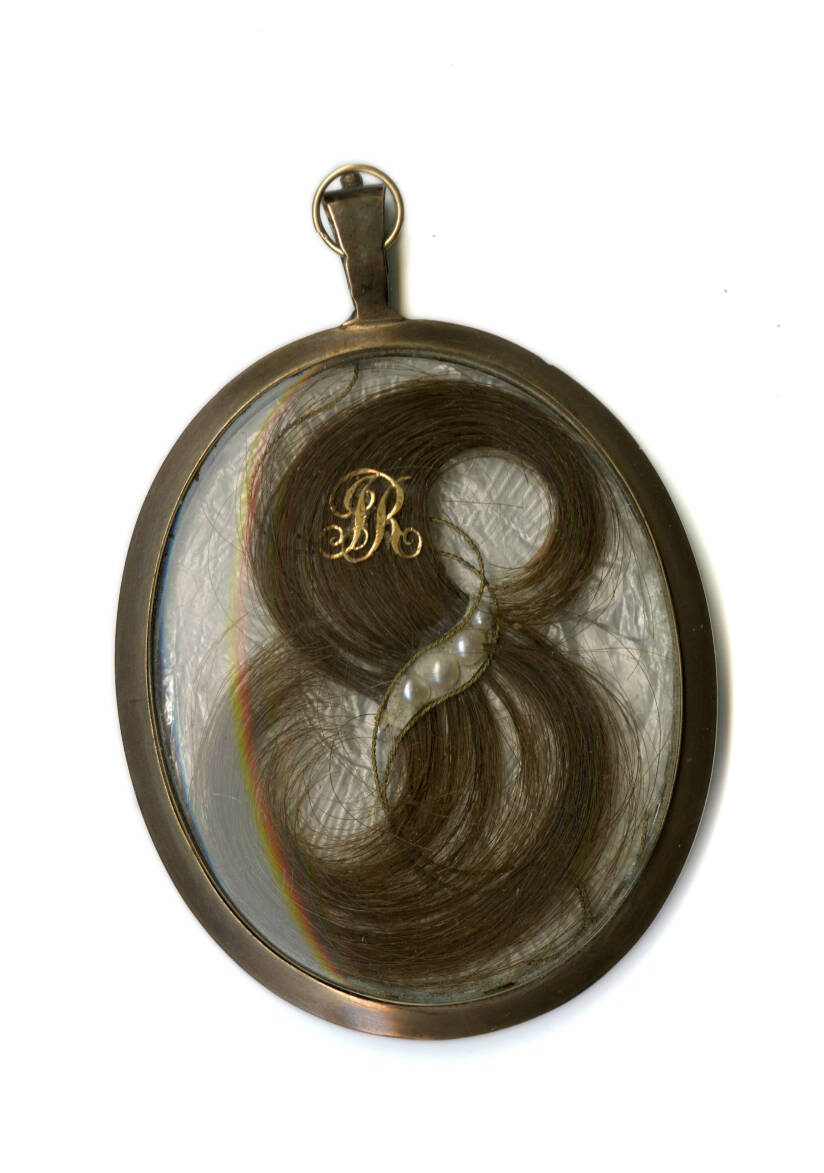 Metal pendant with a glass ocver that holds tiny pearls and a lock of hair.